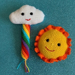 May include: A crocheted rainbow cloud with a smiling face and a crocheted yellow sun with a smiling face.