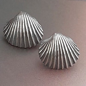Puede incluir: Un par de pendientes de plata en forma de concha. Los pendientes están hechos de metal y tienen un diseño detallado y texturizado.