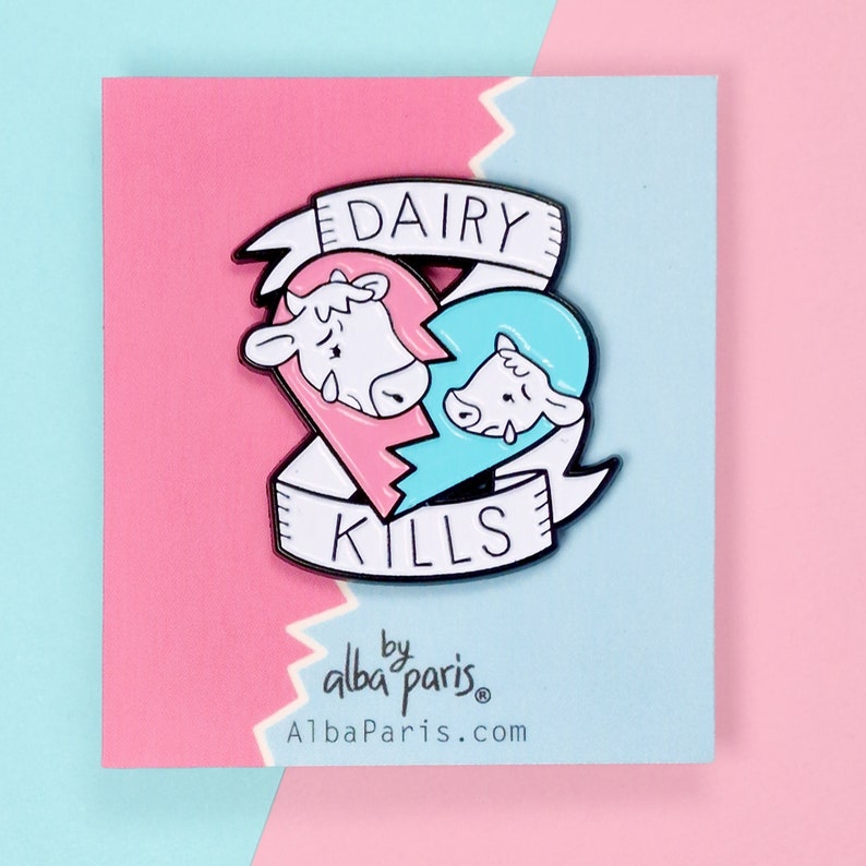 Alba Paris pin / badge of a broken heart, half pink with the face of a mother cow and the other half blue with the face of a male calf. Both are crying because they are being separated. And a white ribbon, with a message that reads Dairy Kills.