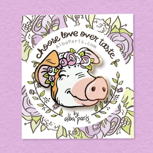 Könnte beinhalten: Eine goldfarbene Emaille-Anstecknadel mit einem Cartoon-Schwein, das eine Blumenkrone trägt. Das Schwein lächelt und hat eine rosa Nase. Die Anstecknadel ist von einem Kreis mit dem Text "Choose love over taste" und "AlbaParis.com" umgeben. Der Text "by alba paris" ist ebenfalls unter dem Schwein enthalten.