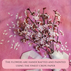 Puede incluir: Un ramo de delicadas flores de papel blanco con tallos marrones y p&eacute;talos rosados. Las flores est&aacute;n hechas a mano y pintadas con el mejor papel crep&eacute;. Las flores est&aacute;n dispuestas sobre un fondo rosa con p&eacute;talos de papel blanco esparcidos.