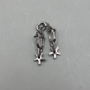 Op de afbeelding: Een paar kleine, zilverkleurige sporen verbonden door een ketting. Elke spoor heeft een gebogen lichaam en een stervormige spoorwiel. De sporen zijn ontworpen om te paardrijden en zijn waarschijnlijk van metaal.