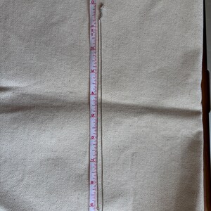 May include: A silver necklace with a small pendant, approximately 10 inches long, is displayed on a beige fabric. A measuring tape is placed next to the necklace, showing its length in inches.