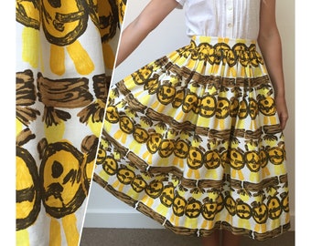 May include: A white skirt with a brown and yellow pattern of stylized faces. The skirt is full and has a gathered waistband.