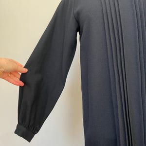 May include: A long-sleeved, navy blue dress with a pleated front. The dress has a simple, classic design and is made of a soft, comfortable fabric.