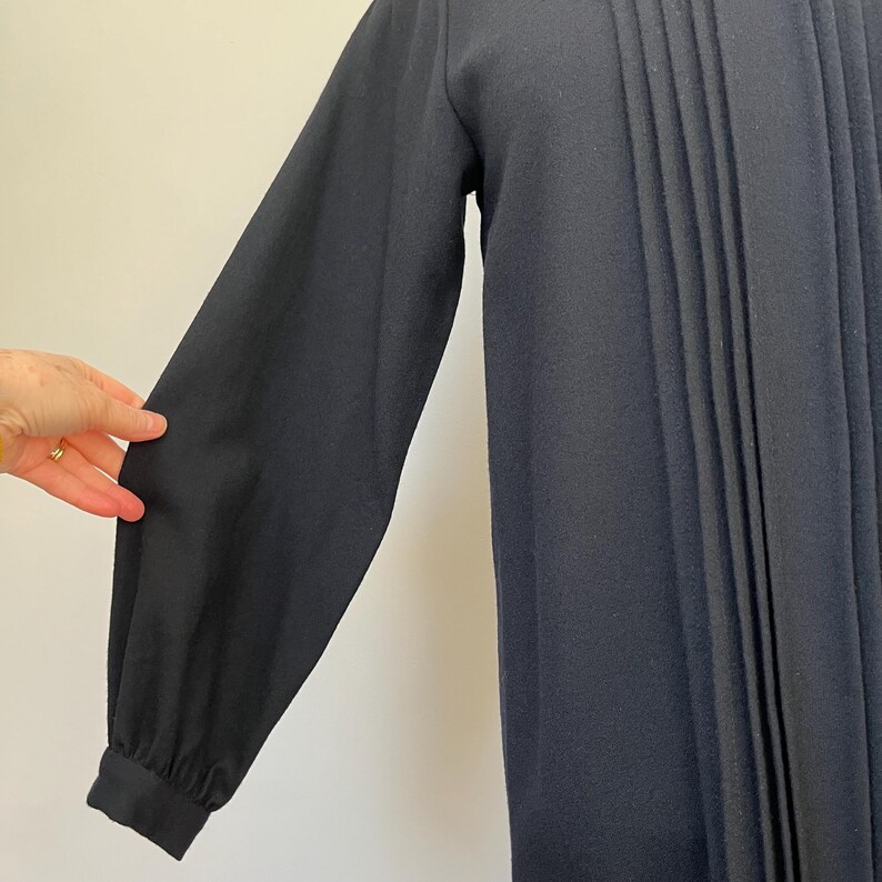 May include: A long-sleeved, navy blue dress with a pleated front. The dress has a simple, classic design and is made of a soft, comfortable fabric.