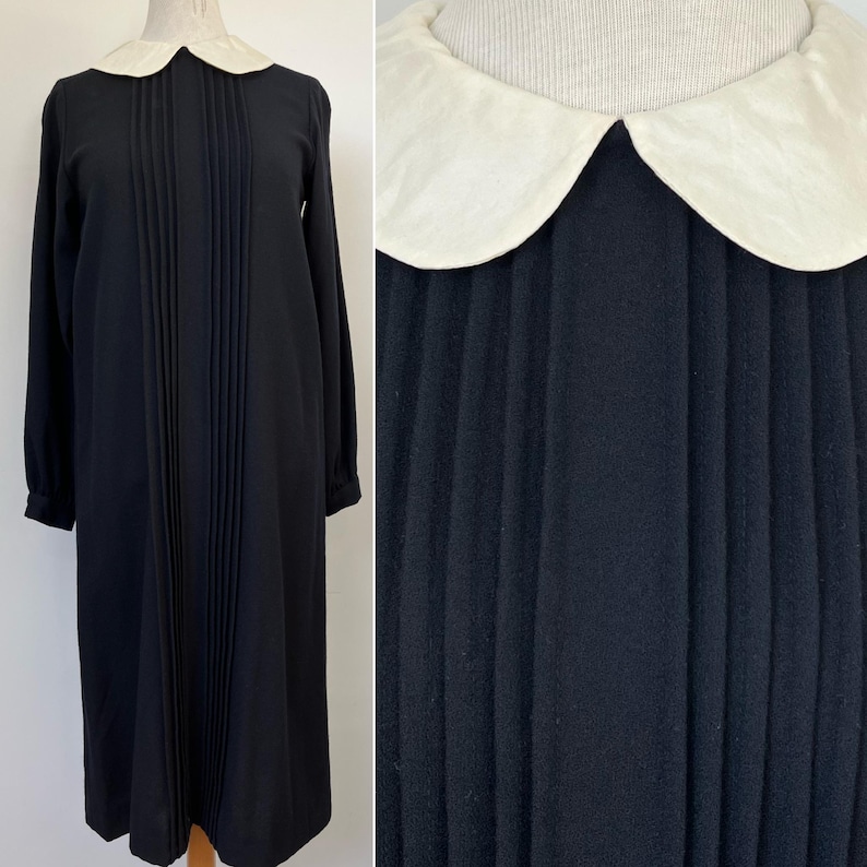 May include: A black dress with a white Peter Pan collar and vertical pleats. The dress has long sleeves and a midi length.