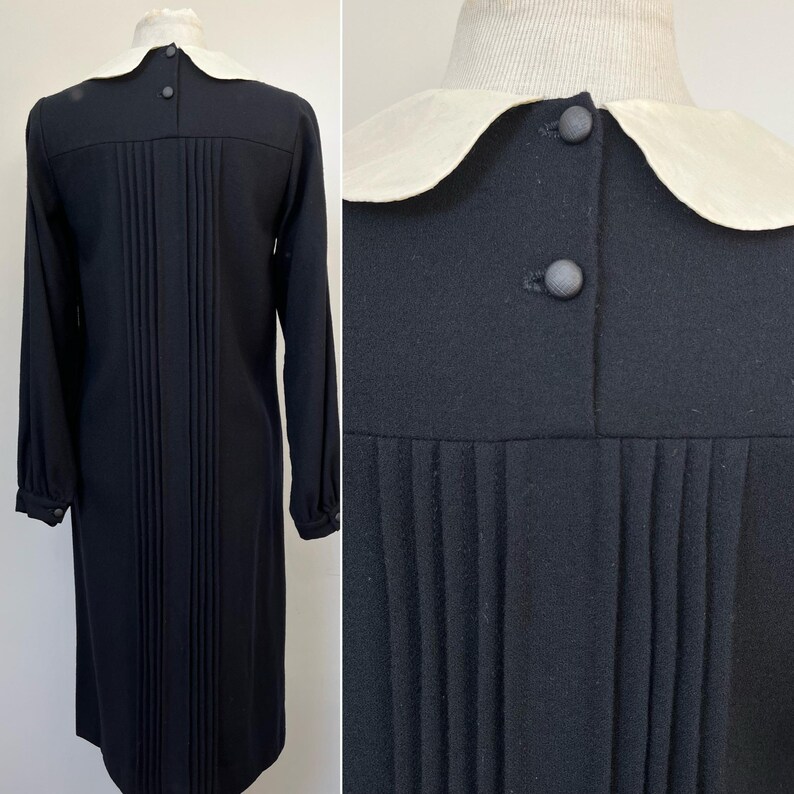 May include: A black long-sleeved dress with a white Peter Pan collar and a row of buttons down the front. The dress has a pleated skirt and is made of a soft, textured fabric.