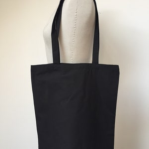 Puede incluir: Una bolsa de tela negra con dos asas largas. La bolsa est&aacute; hecha de una tela lisa y s&oacute;lida.