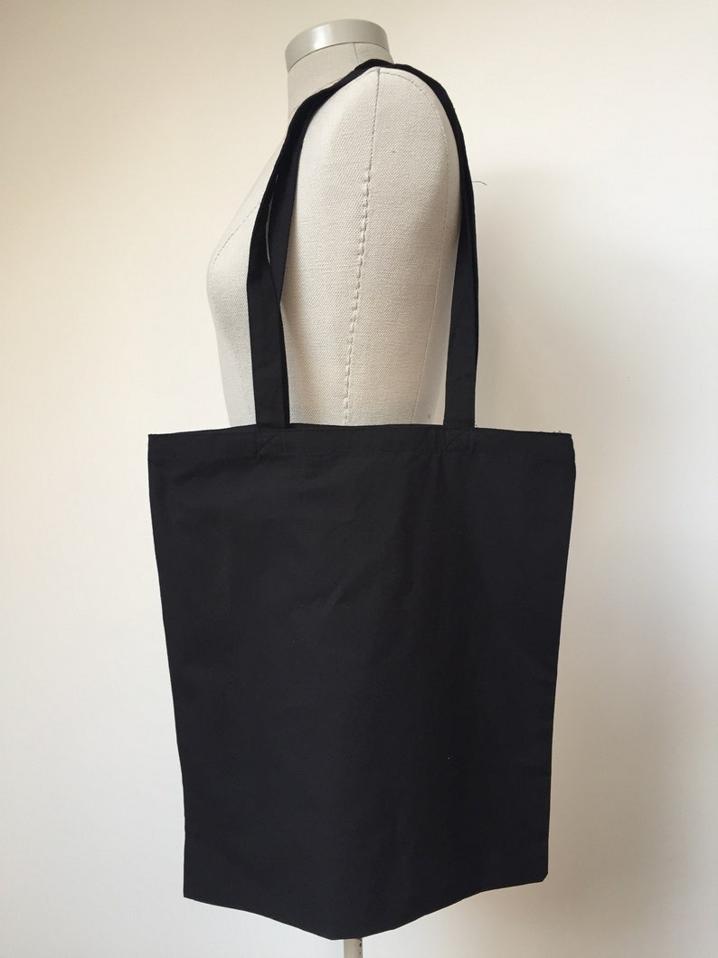 Puede incluir: Una bolsa de tela negra con dos asas largas. La bolsa est&aacute; hecha de una tela lisa y s&oacute;lida.
