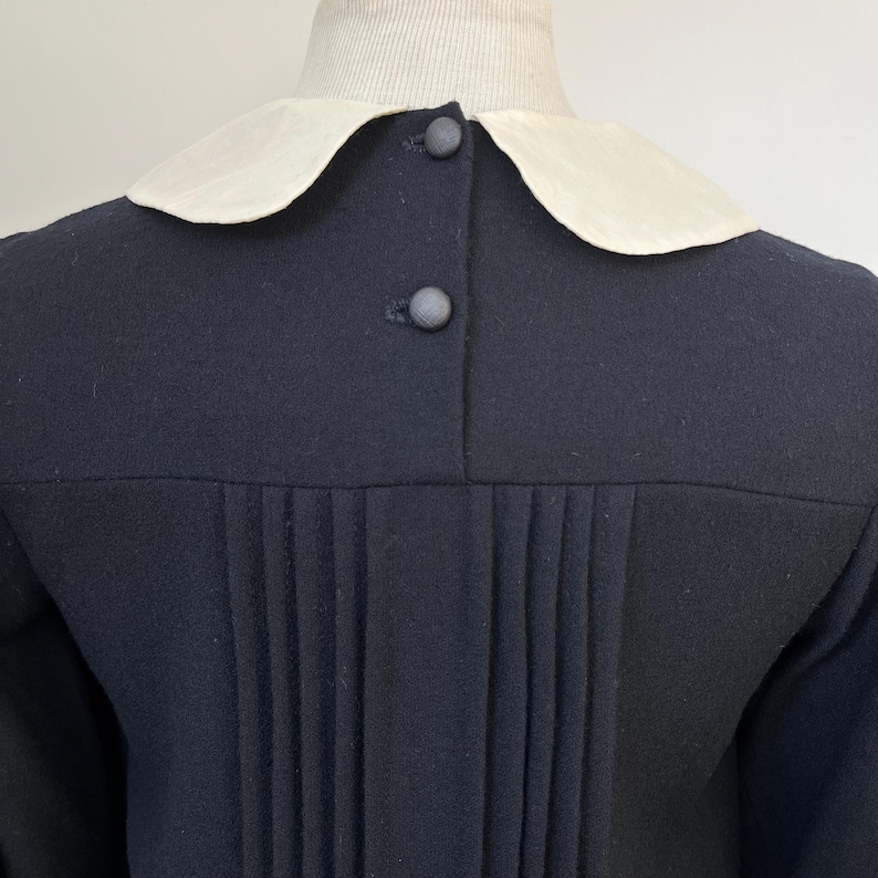 May include: A black dress with a white Peter Pan collar and a row of buttons down the back. The dress has pleats in the skirt.