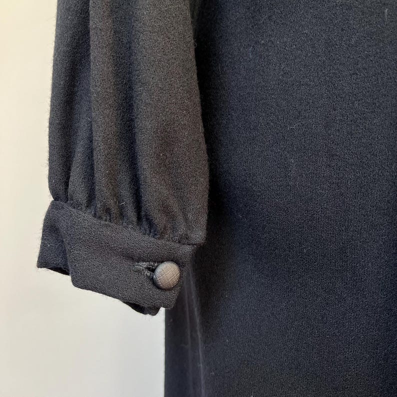 May include: Black long-sleeved dress with a button on the sleeve.