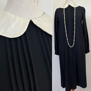 May include: A black midi dress with a white Peter Pan collar and long sleeves. The dress has a pleated skirt and is adorned with a pearl necklace.