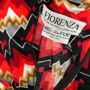 Może przedstawiać: Zbliżenie na czerwoną, czarną, białą i złotą tkaninę w geometryczny wz&oacute;r z białą metką z napisem "Fiorenza Custom Tailored Hong Kong 100% Acrylic Machine Wash Warm Gentle Line Dry".