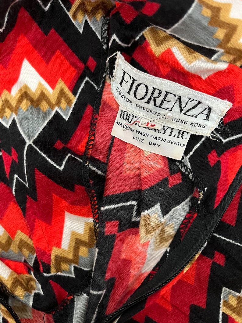 Może przedstawiać: Zbliżenie na czerwoną, czarną, białą i złotą tkaninę w geometryczny wz&oacute;r z białą metką z napisem "Fiorenza Custom Tailored Hong Kong 100% Acrylic Machine Wash Warm Gentle Line Dry".