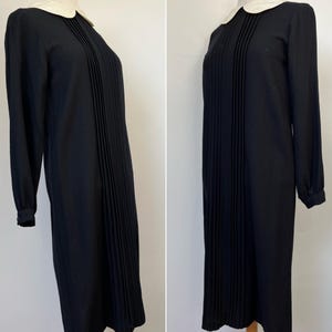 May include: A black pleated dress with a white Peter Pan collar and long sleeves.