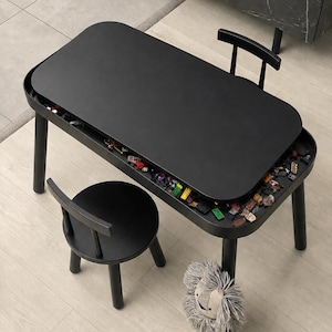 May include: A black rectangular activity table with rounded corners and a removable top, featuring a recessed storage compartment filled with small colorful plastic building blocks. A matching black chair with a round seat is positioned nearby.