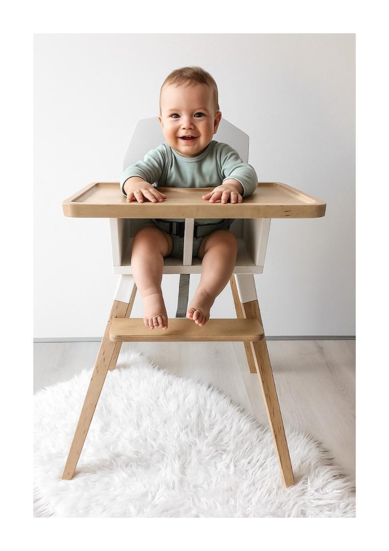 Op de afbeelding: Een lachende baby zit in een houten kinderstoel met een licht dienblad en witte accenten. De kinderstoel heeft een natuurlijke houten afwerking en staat op een zacht wit tapijt. De baby draagt een lichtgroen shirt met lange mouwen.
