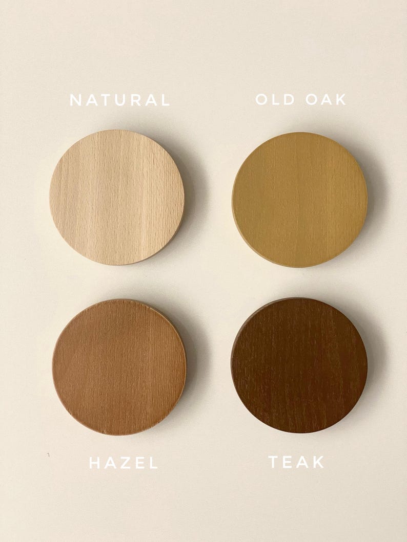 May include: Four circular wooden discs arranged in a grid, each displaying a different wood stain color. The labels read Natural, Old Oak, Hazel, and Teak. Each disc shows a distinct wood grain pattern, ranging from light beige to dark brown tones.