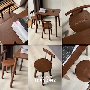 May include: A dark brown wooden table and two matching chairs with circular seats and curved backrests. The seats are engraved with the names Beauden and Oiya. The text WOOD TONE TEAK 3442 H 46 is visible on one of the chair seats.