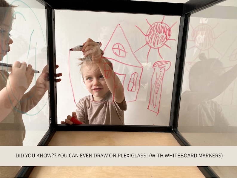 May include: A clear plexiglass cube with a black frame and a light wood base. The transparent panels feature red and green marker drawings of a house and sun. The text on the image reads: DID YOU KNOW?? YOU CAN EVEN DRAW ON PLEXIGLASS! (WITH WHITEBOARD MARKERS)