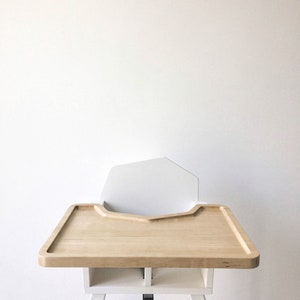 Op de afbeelding: Een moderne kinderstoel met een licht houten blad en witte accenten. De stoel heeft een witte rugleuning en een veiligheidsriem. De poten zijn wit met voeten in natuurlijk hout. De lade is ongeveer 51 cm breed.