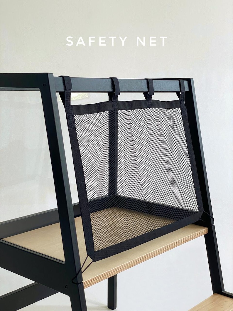 May include: A black mesh safety net attached to a black wooden frame with light wood shelving. The text SAFETY NET is printed in white above the mesh. The net features black fabric borders and is secured with straps to the top horizontal bar.