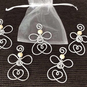 Può includere: Cinque ornamenti a forma di angelo in filo d'argento con teste di perline di legno e corpi a forma di cuore sono esposti su una superficie marrone. Sullo sfondo c'è un sacchetto trasparente bianco con coulisse. Gli angeli hanno un aspetto stravagante e fatto a mano.