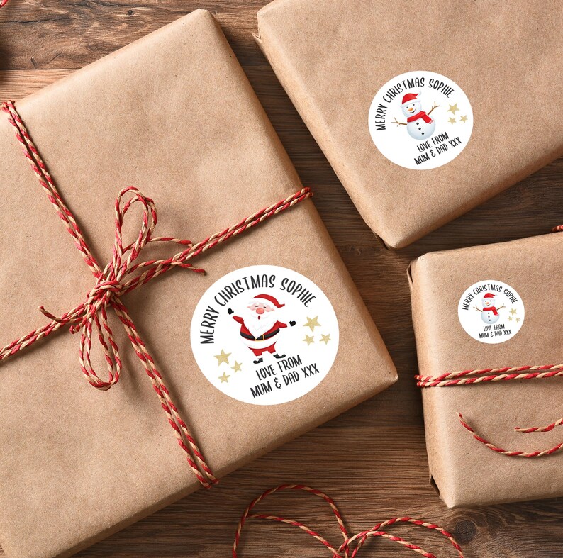 Op de afbeelding: Cadeaus verpakt in bruin papier en vastgebonden met rood en wit touw. Elk pakket heeft een ronde sticker met de tekst "Merry Christmas Sophie" en feestelijke illustraties.
