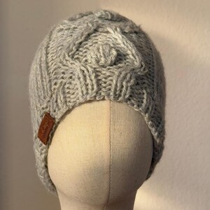 May include: A gray knitted beanie with a cable knit pattern. The beanie has a leather label with the text "L.L.Bean" on it.