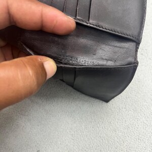 May include: A dark brown leather wallet featuring multiple interior card slots and a visible serial number embossed on the inner fold reading 035 2184 2151 5. The wallet has a smooth texture and a structured design with visible stitching along the edges.