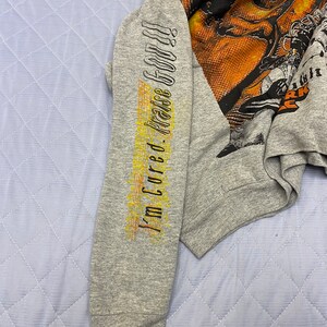 May include: A heather gray long-sleeve sweatshirt featuring a large, multi-colored graphic print on the chest and the text "I'm Cured. Praise God!!" printed vertically in black and yellow along the length of the left sleeve.
