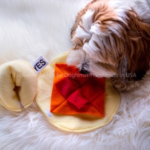 May include: A yellow and orange dog toy with a red and orange square in the centre. The toy is made of soft fabric and is designed to be durable. The toy is labelled "YES" and "Exclusive design by DogNmat - Handmade in USA".