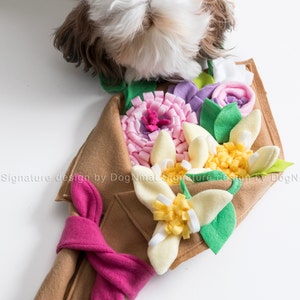 May include: A brown felt dog toy shaped like a bouquet of flowers. The flowers are made of felt and include yellow, pink, and purple flowers with green leaves. The toy is tied with a pink ribbon.