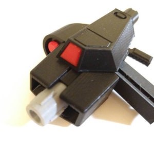 May include: A black plastic toy gun with a red button and a gray barrel. The gun has a futuristic design and is made of 3D printed plastic.