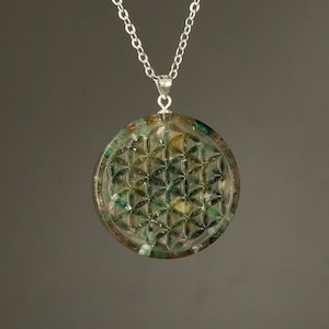 Puede incluir: Un collar de cadena de plata con un colgante de flor de la vida verde y dorado.