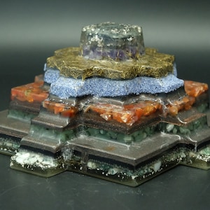 May include: A multi-layered crystal pyramid with a gold, purple, blue, red, green, and black color scheme. The pyramid is made of various crystals and stones.