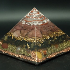 May include: A clear pyramid with layers of different colored crystals and gold leaf. The crystals include rose quartz, amethyst, clear quartz, and citrine.