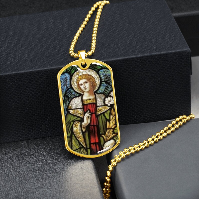 Puede incluir: Collar de cadena dorada con un colgante de placa de identificaci&oacute;n dorada con una imagen de vitral de un &aacute;ngel con alas, una t&uacute;nica verde y una faja roja.