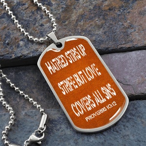 May include: A silver chain necklace with a brown dog tag pendant. The dog tag has white text that reads "Hatred stirs up strife but love covers all sins Proverbs 10:12".