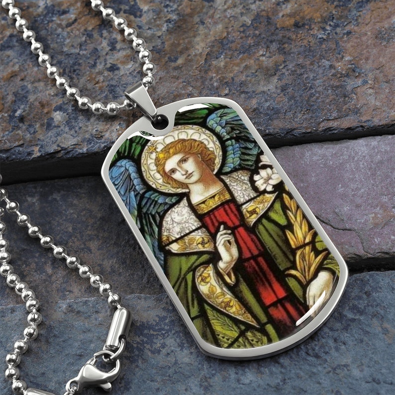 Puede incluir: Un collar de cadena plateada con un colgante de placa de identificaci&oacute;n de acero inoxidable con una imagen de vitral de un &aacute;ngel con alas, un halo y una t&uacute;nica verde y roja.