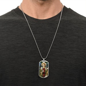 Puede incluir: Un collar de cadena de plata con un colgante de placa de identificaci&oacute;n de plata que presenta una imagen de vitral de un &aacute;ngel con alas, un halo y una t&uacute;nica roja.