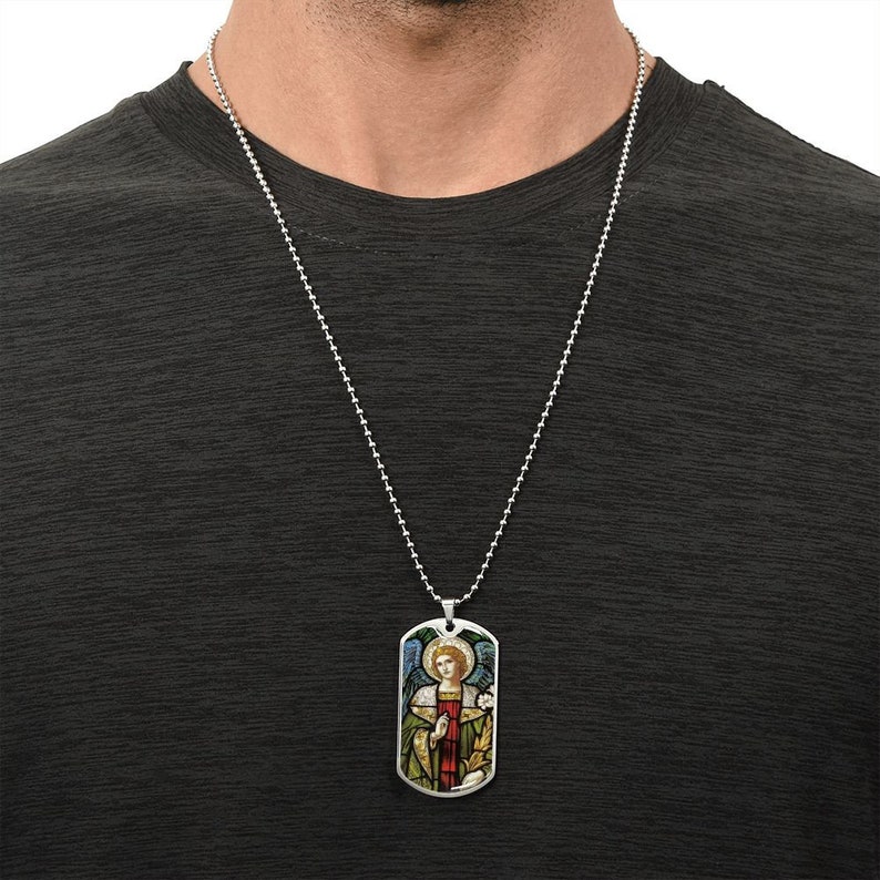 Puede incluir: Un collar de cadena de plata con un colgante de placa de identificaci&oacute;n de plata que presenta una imagen de vitral de un &aacute;ngel con alas, un halo y una t&uacute;nica roja.