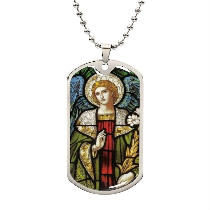 Puede incluir: Un collar con una placa de identificaci&oacute;n de perro de plata con una imagen de vitral de un &aacute;ngel con alas, un halo y una t&uacute;nica verde y roja. El &aacute;ngel sostiene una rama con hojas.