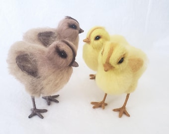 May include: A group of four felted chicks. Two are light brown with darker brown wing markings, and two are yellow with light brown accents. The chicks have black eyes and stand on wire legs. The background is white.