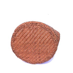 May include: A round, woven basket with a natural brown color. The basket is made of tightly woven fibers, creating a textured surface. The basket's shape is circular, with a slightly curved side.