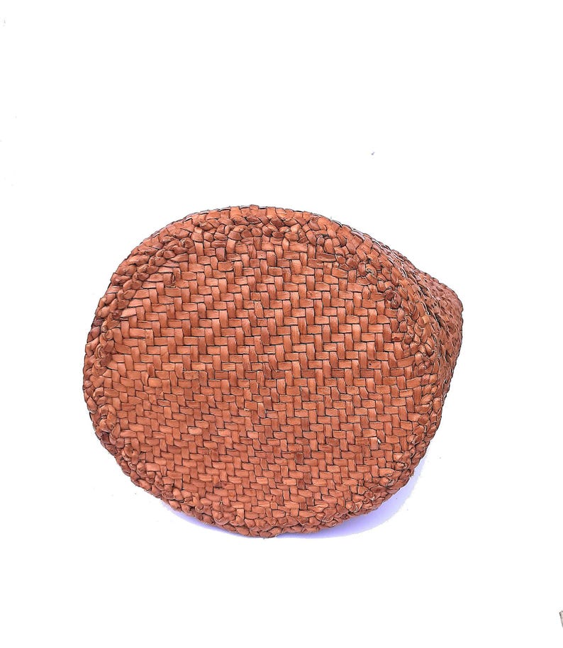 May include: A round, woven basket with a natural brown color. The basket is made of tightly woven fibers, creating a textured surface. The basket's shape is circular, with a slightly curved side.