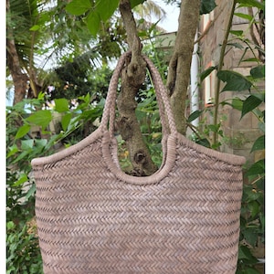 Peut inclure: Un sac fourre-tout tissé de couleur taupe neutre est suspendu à une branche d'arbre. Le sac présente un motif de tissage en panier et des poignées tressées. Le design à dessus ouvert et l'intérieur spacieux le rendent adapté à divers usages.