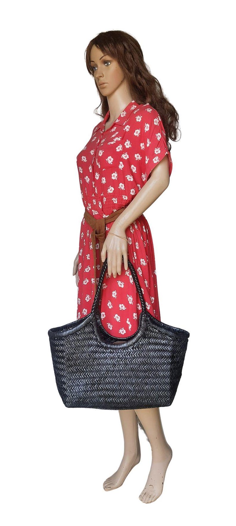 May include: A black woven tote bag with a braided handle. The bag is held by a mannequin wearing a red dress with white floral patterns and a brown belt. The bag's dimensions are approximately 18 inches wide and 12 inches tall.