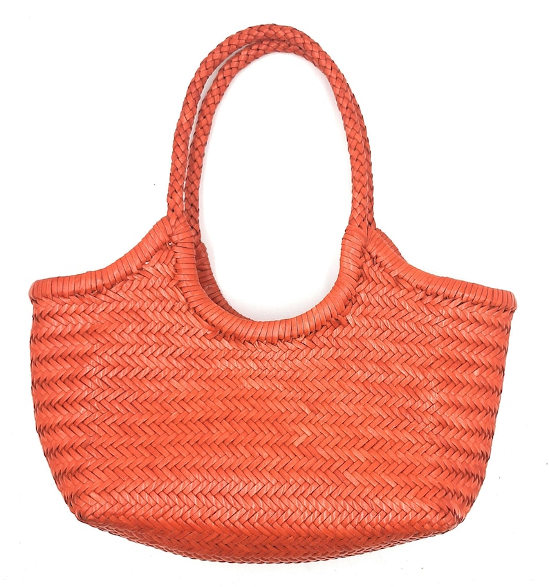 May include: A woven orange tote bag with braided handles. The bag features a basket weave pattern and a rounded shape. The handles are thick and sturdy, designed for comfortable carrying. The bag is made of a durable material.